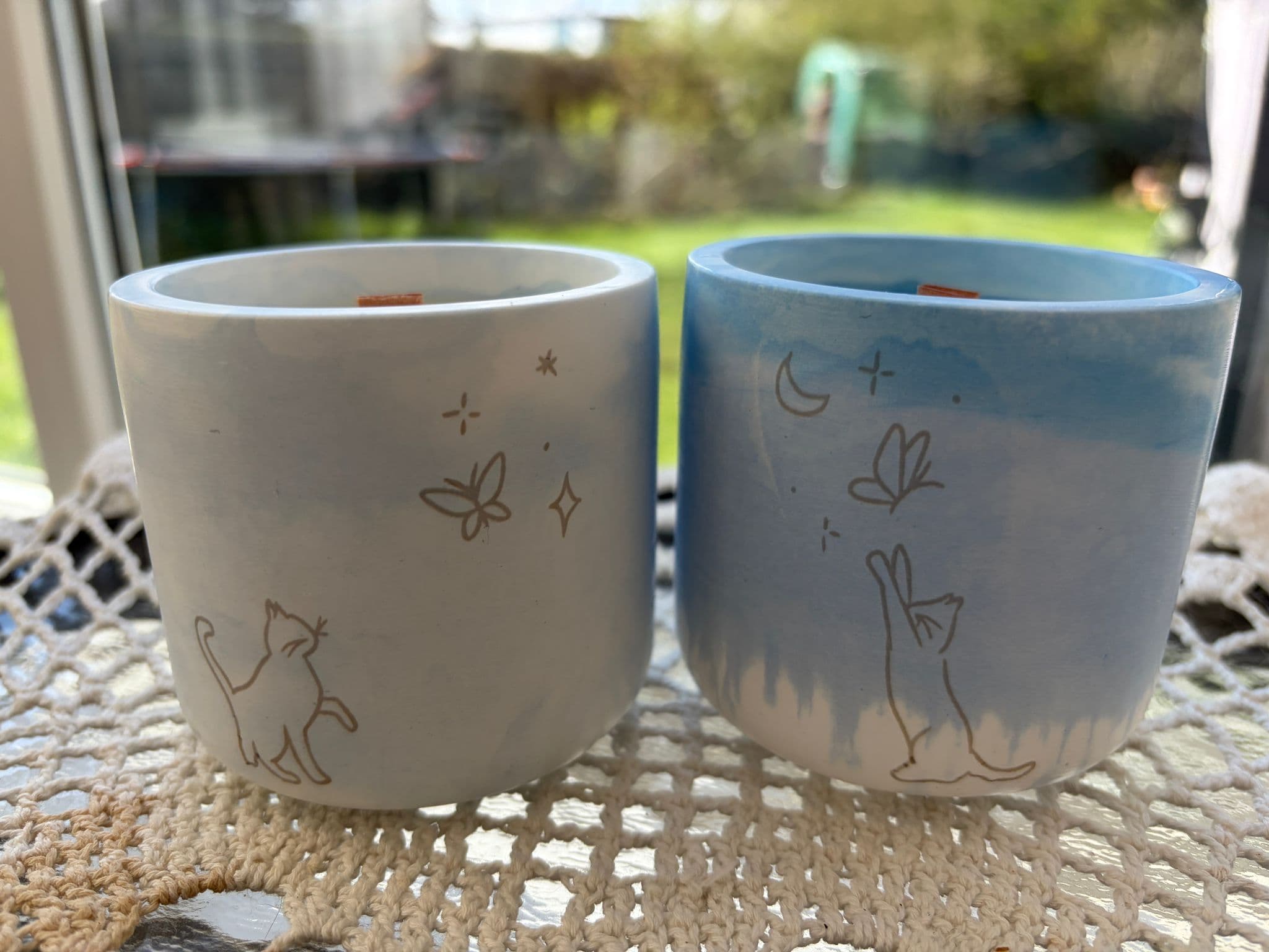 Soft blue and cream ceramic candles with cat, butterfly, moon, and star line art